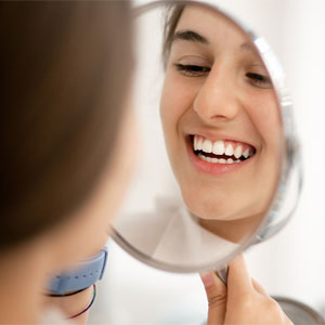 Patient smiling and looking at the mirror to see her smile makeover at Fairbanks Periodontal Associates in Fairbanks, AK