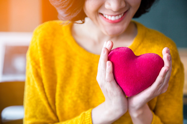 A woman smiling and holding a felt heart from Fairbanks Periodontal Associates in Fairbanks, AK